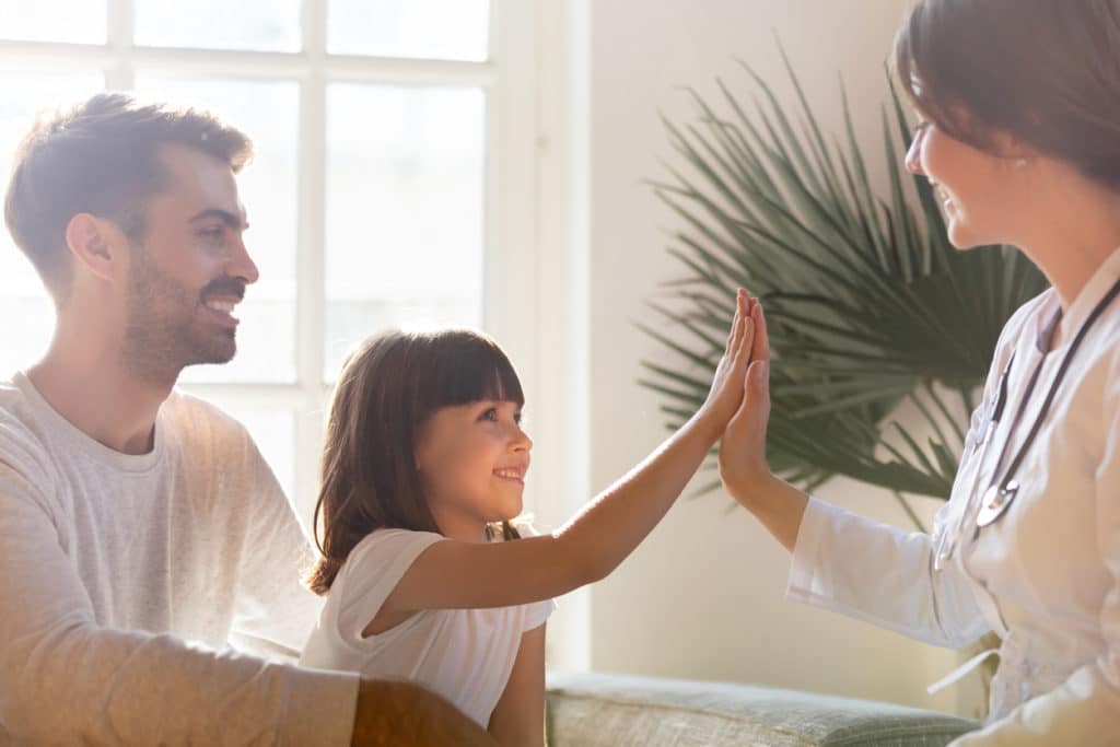 Smiling preschooler girl with young dad give high five to visiting doctor or nurse, happy father with little daughter make deal with pediatrician to follow healthy lifestyle. Healthcare concept