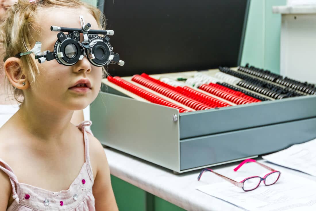 Young girl stand still while undergoing eye test with phoropter.