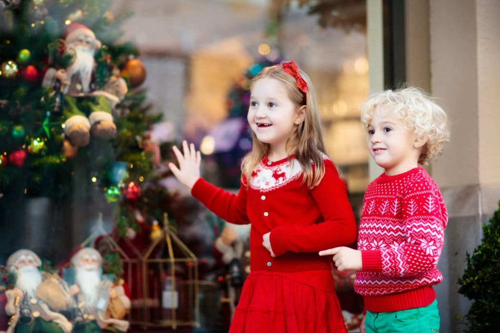 Kids shopping for Christmas presents. Children buy Xmas decoration and tree. Little girl and boy at decorated shop window with lights and Santa toys. Family buying Christmas gifts. Winter holidays.