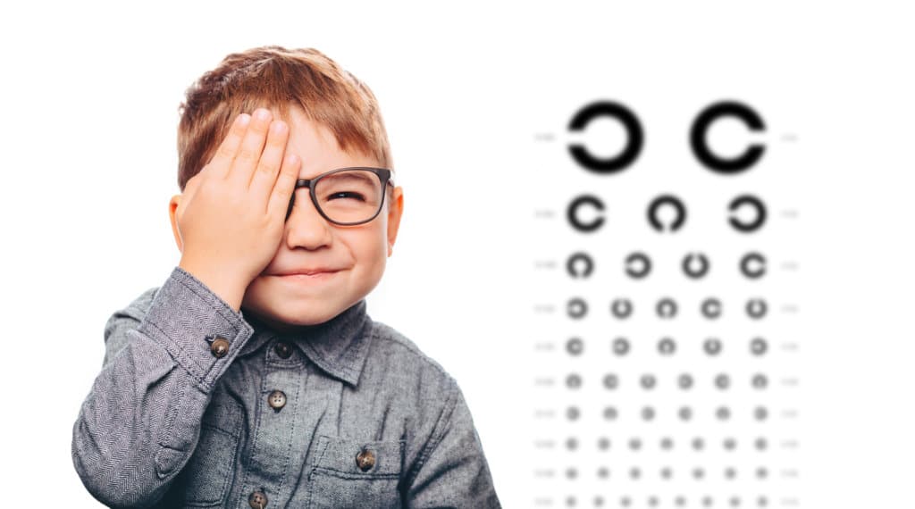 boy having eye exam with eye chart and covering one eye.