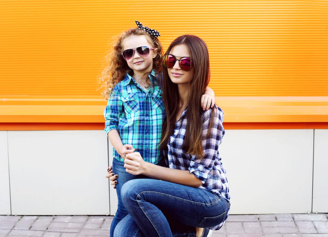 Fashion family concept - stylish mother and child wear a checkered shirts and sunglasses in the city together against the colorful wall