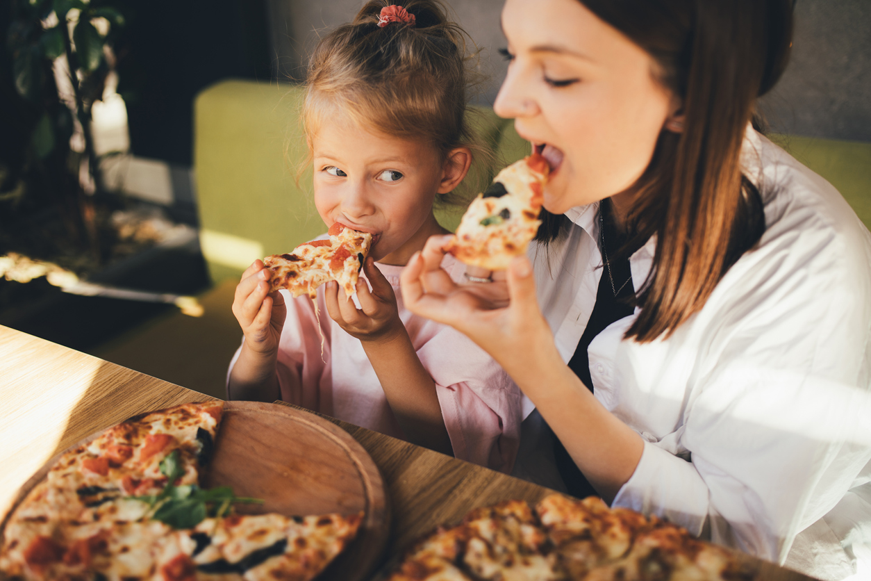 Happy mother and daughter eat pizza in a cafe and having fun.