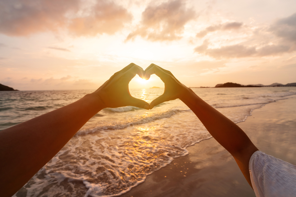 Young couple traveler making heart shape with hands on the beach at sunset, Lovers on honeymoon and Valentine's day concept