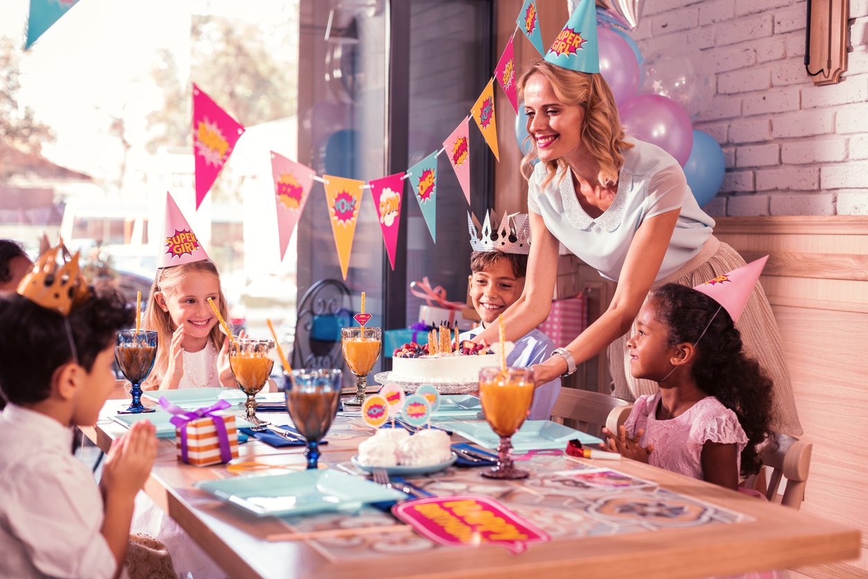 Bringing cake. Cheerful loving mother smiling and putting birthday cake on the table for children