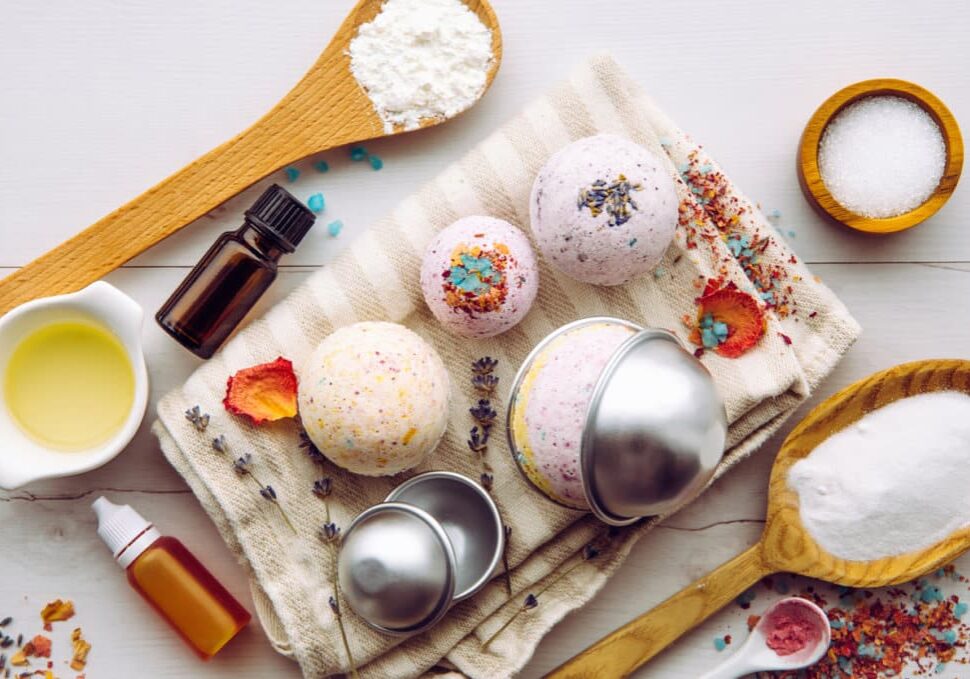 Making bath fizz bombs at home concept. All the ingredients on table on wood spoons: cornstarch, essential oil, dye, citric acid, baking soda, dry herbs, round metal pressing molds.