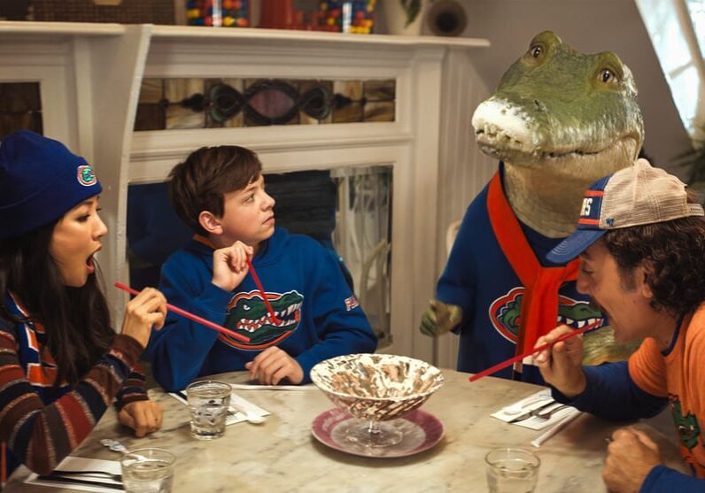 (l to r) Mrs. Primm (Constance Wu), Josh Primm (Winslow Fegley), Lyle (Lyle the Crocodile) and Hector (Javier Bardem) slurp up an ice cream sundae in Columbia Pictures LYLE, LYLE, CROCODILE.  Photo by: Courtesy of Sony Pictures