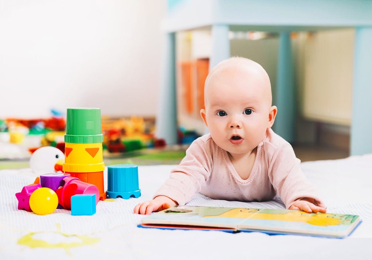 Adorable 6 months old baby looking and reading a book. Baby playing with colorful toys at home. Happy child playing and discovery. Early development, learning and education of kid