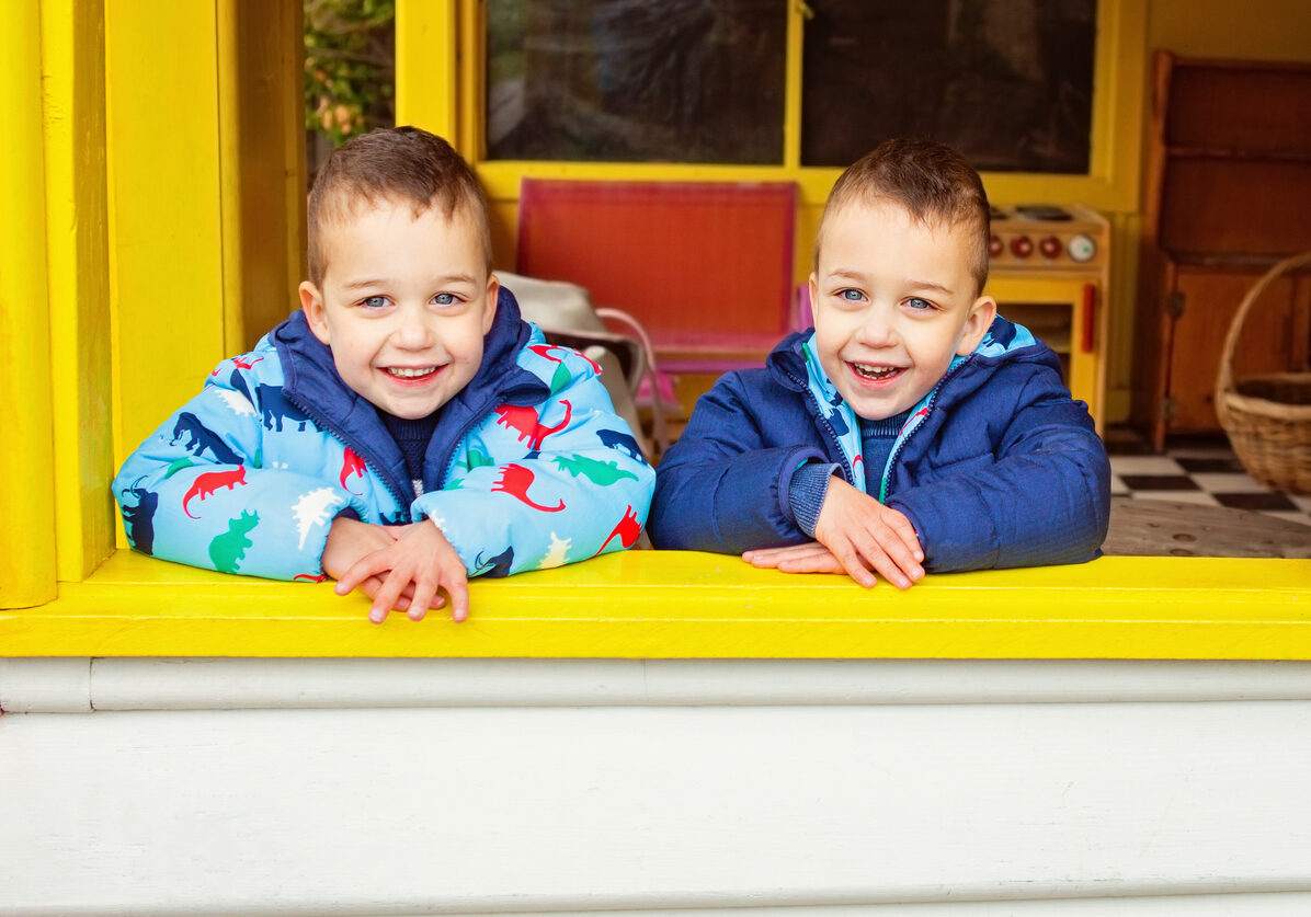 two boys that are twin brothers smiling and leaning on a window opening
