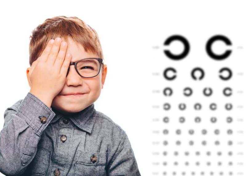 boy having eye exam with eye chart and covering one eye.