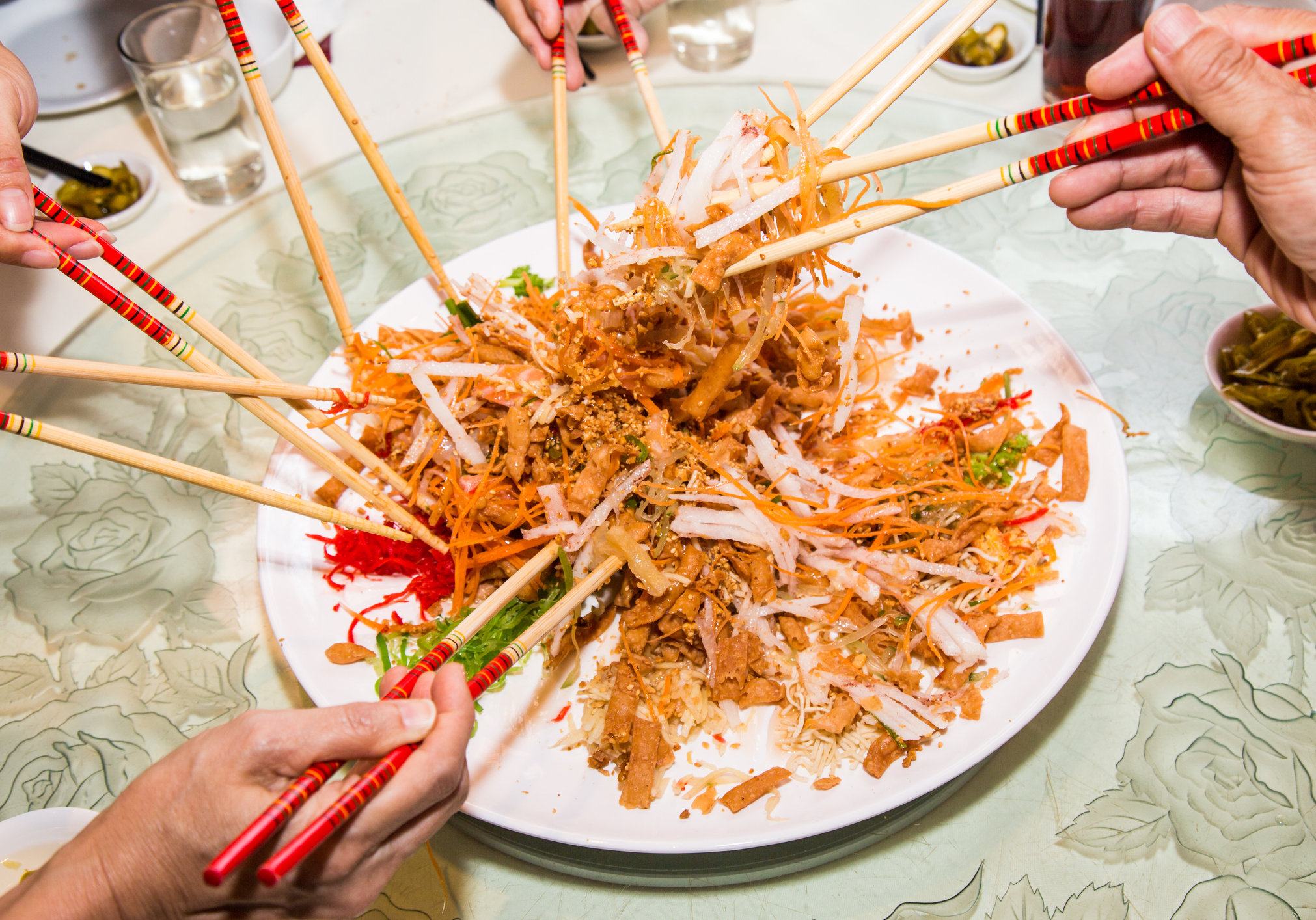 A group of people mixing and tossing Yee Sang dish with chop sticks. Yee Sang is a popular delicacy taken during Chinese New Year, believed to bring good fortune and luck