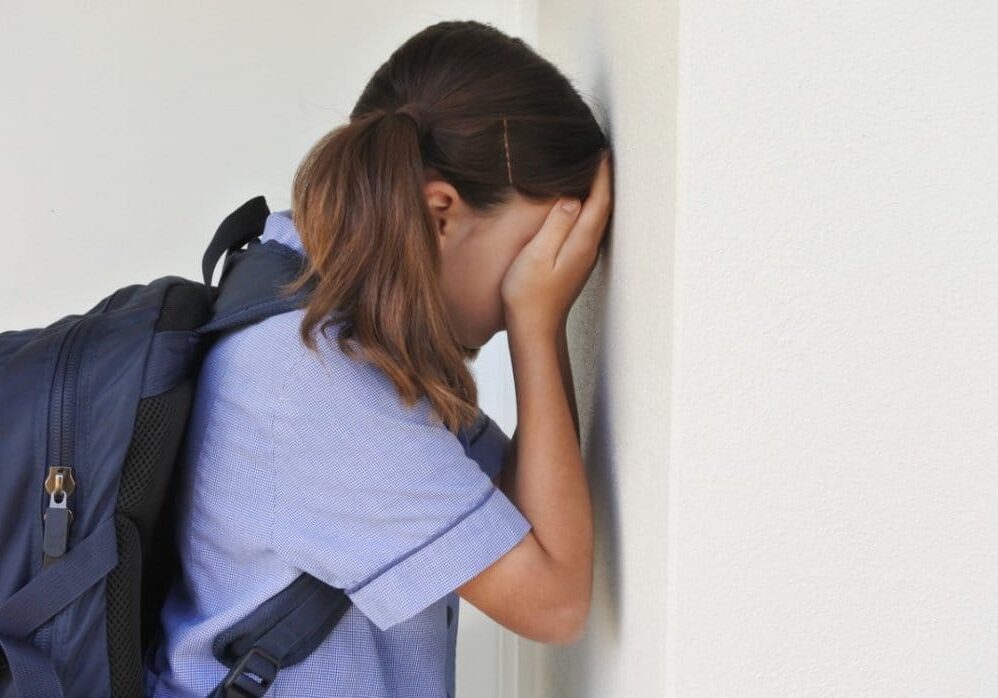 sad-young-schoolgirl-covering-her-face-and-crying-against-a-wall-picture-id1223793020